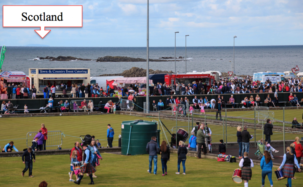 Look Close: The Scottish island, Islay, can be seen just beyond the festivities of the pipe band competition in the Northern Irish town of Portrush.