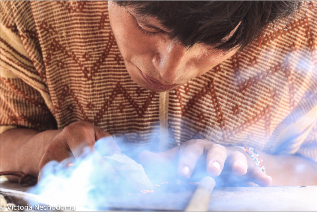 A tribesman in the Peruvian jungle kindles a fire with twigs. Photo by Victoria Nechodomu