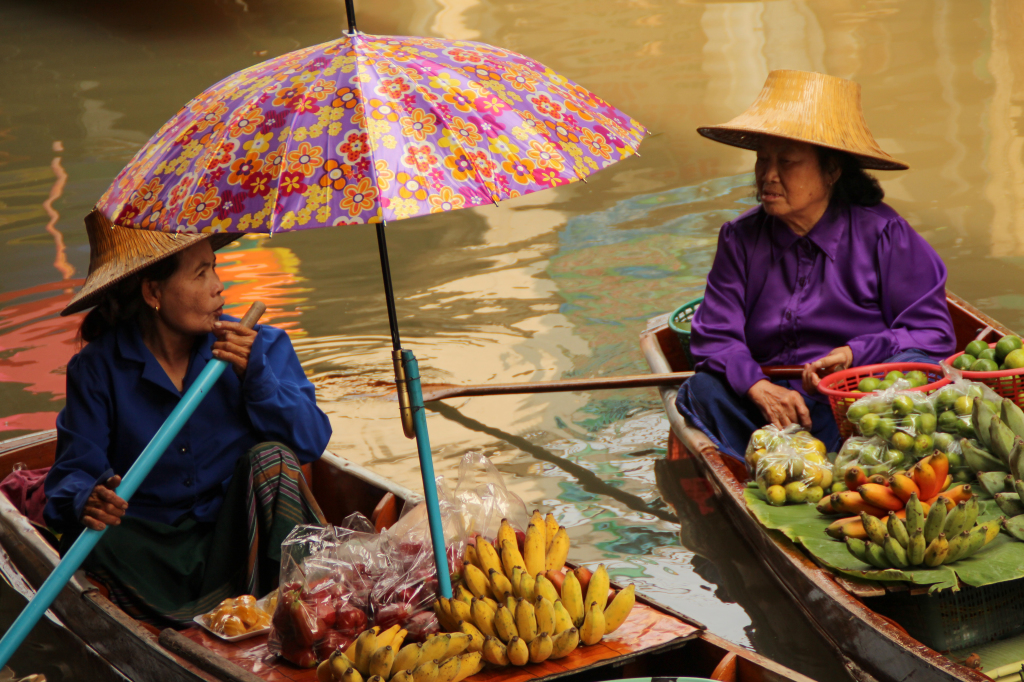 Two fruit vendors visit with one another as they drift in the canal. For many women, the market has become a way of life for them, serving as both a source of income and social time. (Photo by Victoria Nechodomu/Nechodomu Media)