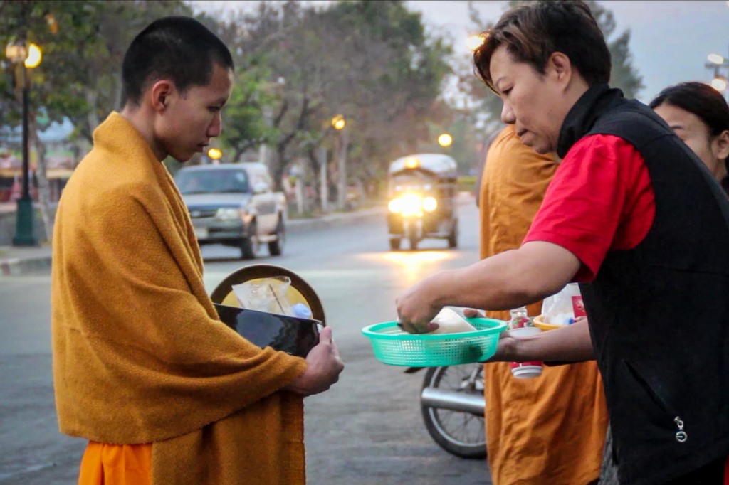 A young monk collects food from devout Buddhists early in the morning in a Chiang Mai market. This act, called “making merit,” is believed to bring happiness and peace to those who give. (photo by Victoria Nechodomu/Nechodomu Media)
